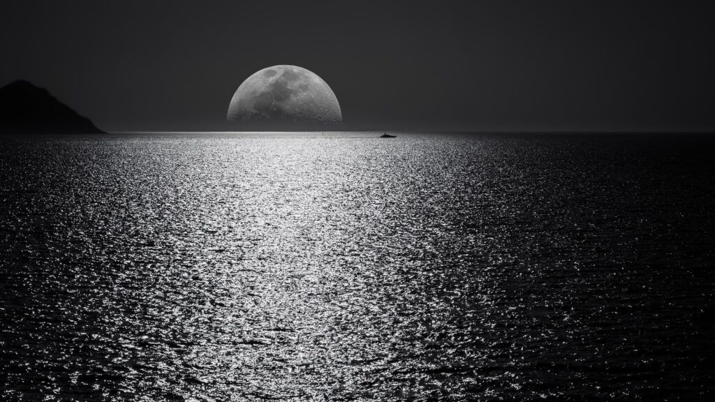 Monochrome image of a boat on the sea next to the shining moon