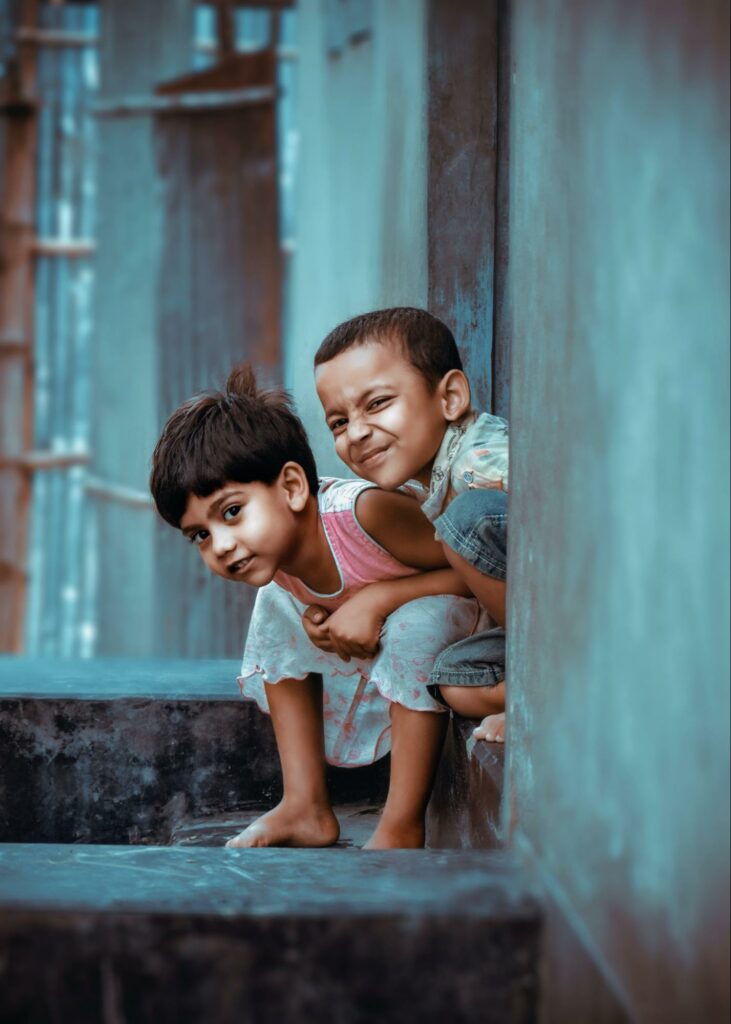 two children sitting outside the house, smiling at the camera