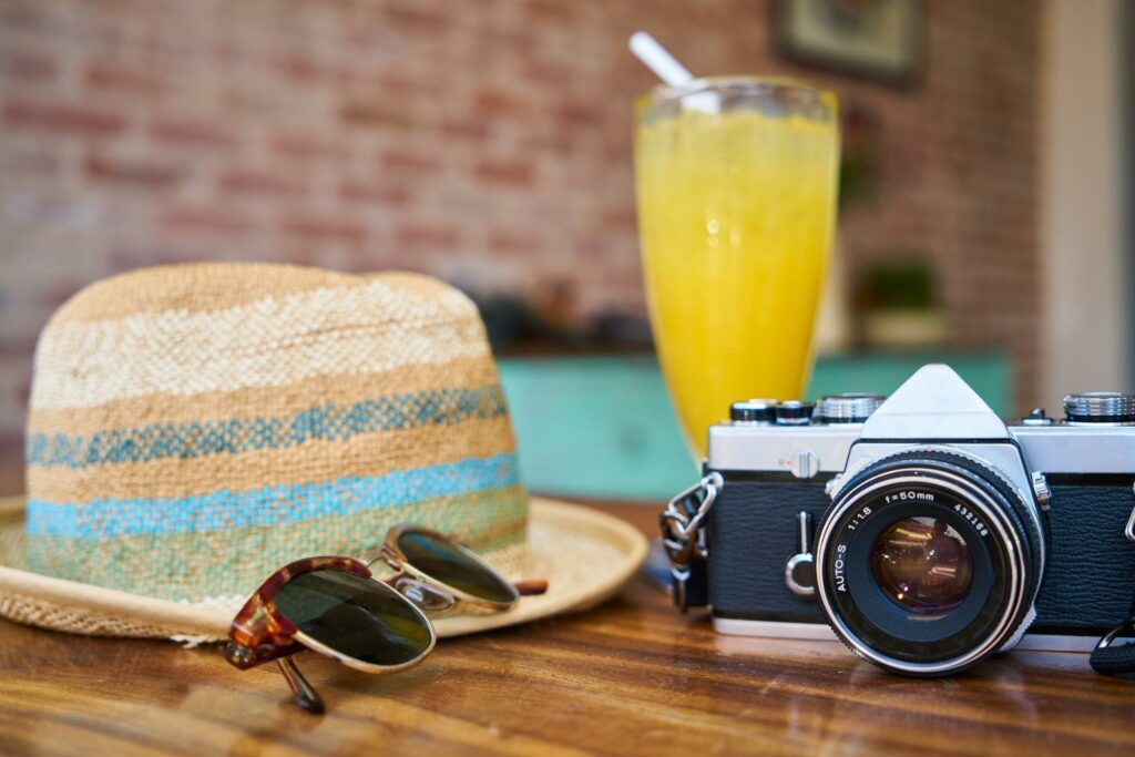 a camera, glasses, straw hat and orange juice on the table