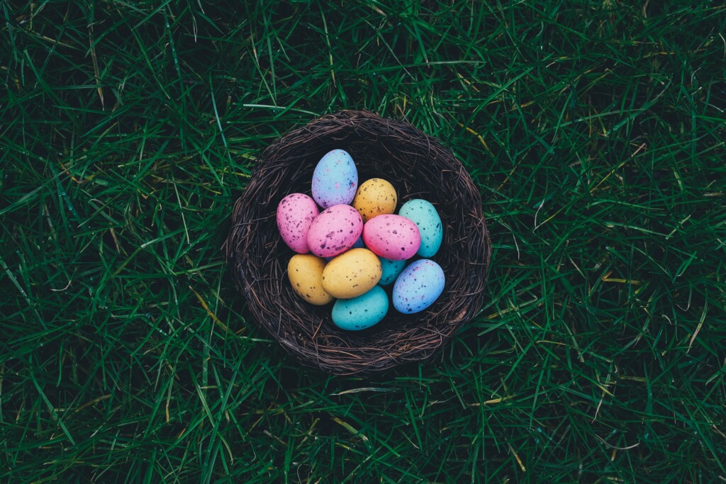 several blue, orange and pink easter pastel eggs in a wooden basket on the grass