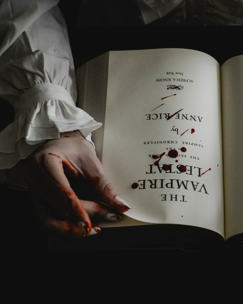a girl reading a book about vampires with blood on her hands and drops of blood on the book.