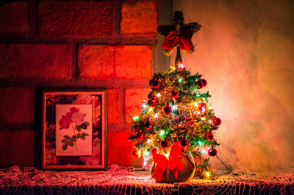A small Christmas tree on a fireplace decorated with red ribbons, red pendants, a string with colored lights, and a golden star topper
