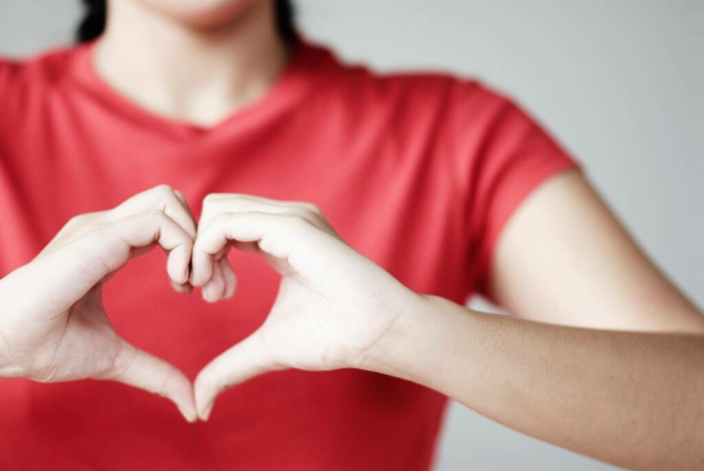 Picture of a girl in a red T-shirt making a heart shape with her hands.
