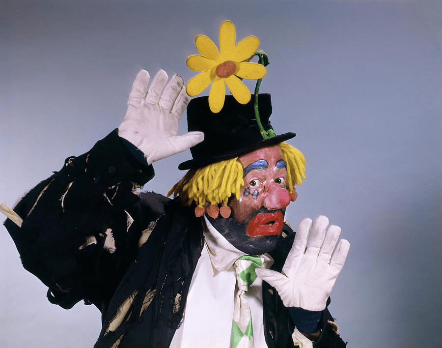 a picture of a character clown with yellow haire, a black hat and dress with a sunflower on his hat